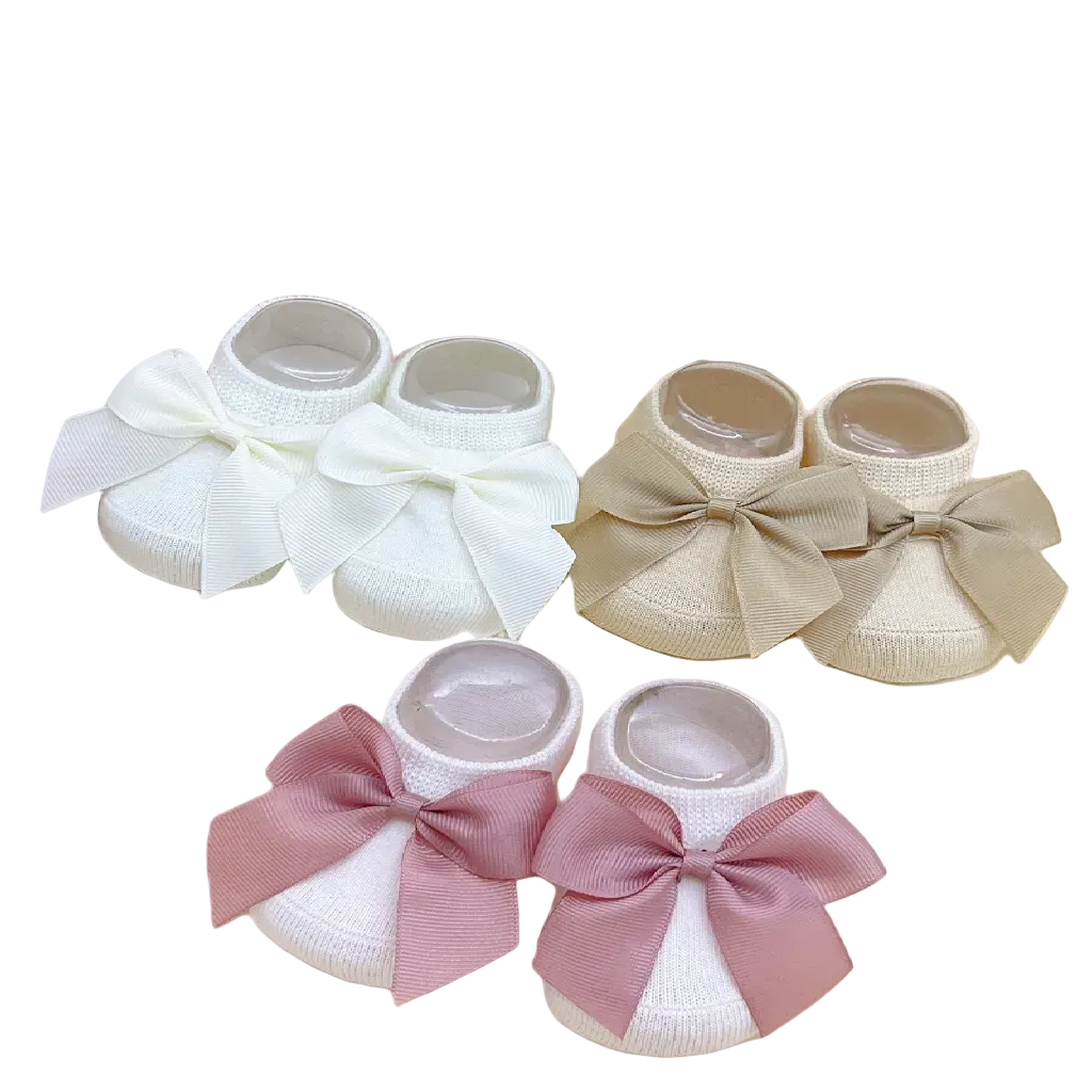 Set of baby shoes with bows in white, beige, and pink on a floral background.