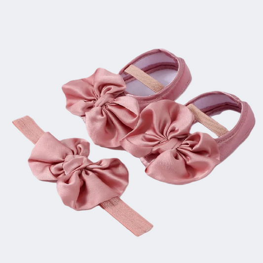 Pink baby shoes with large bows on a white background