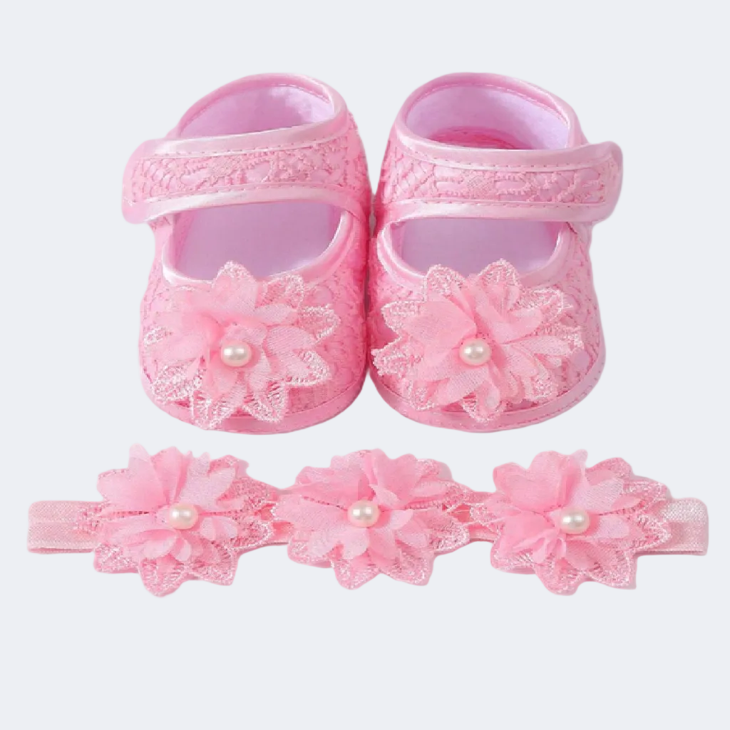Pink baby shoes with floral designs and a matching headband on a white background