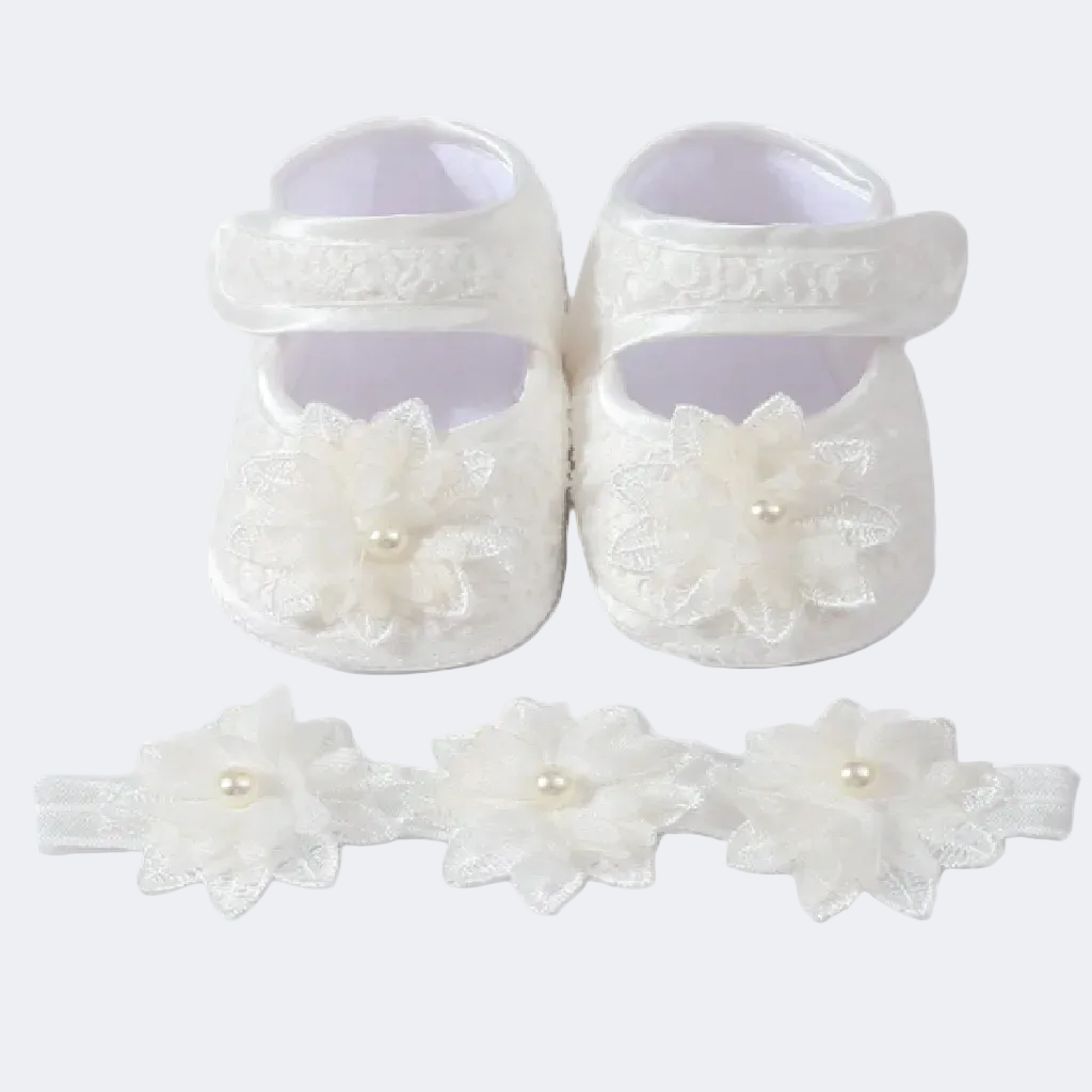 White baby shoes with floral details and a matching headband on a white background