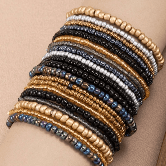 Stack of beaded bracelets in gold, black, and silver on a beige arm.