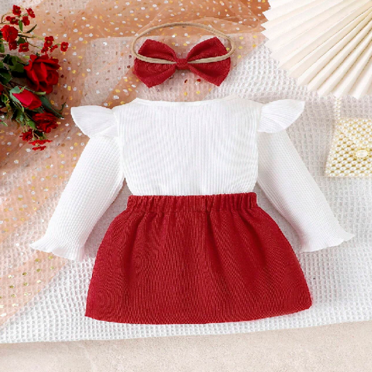 Children's outfit with white top and red skirt on a textured surface.
