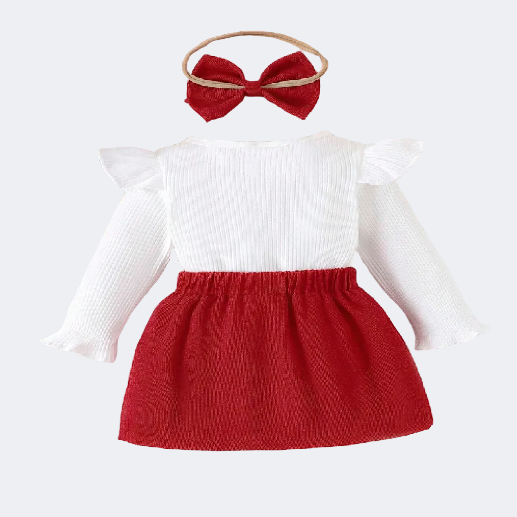 Children's outfit with white top and red skirt on a textured surface.