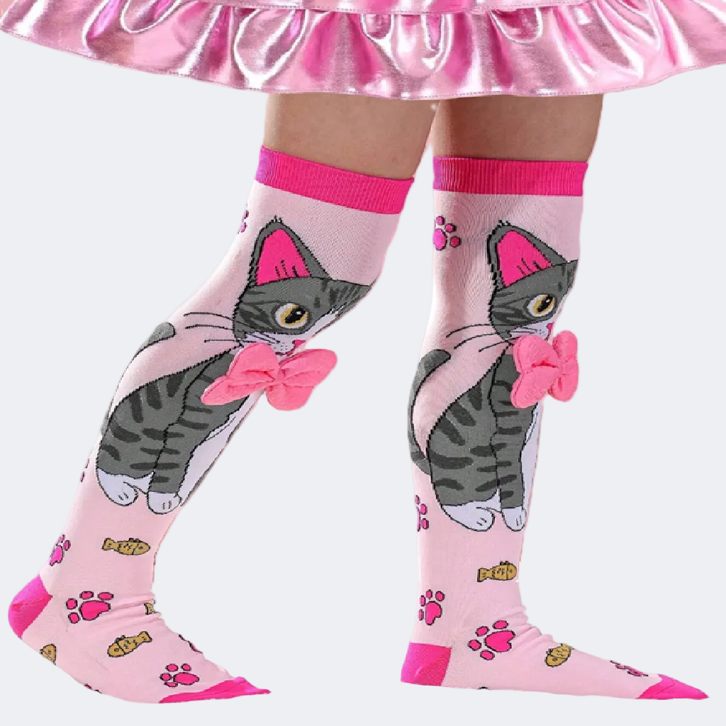 Pink knee-high socks with cat design worn by a person in a pink skirt.