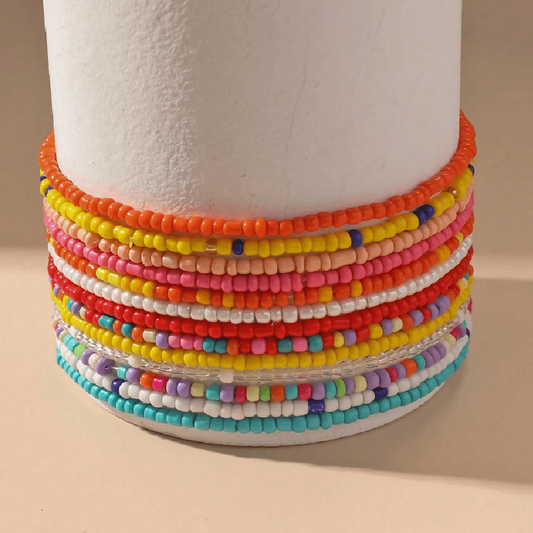 Colorful beaded anklets on a foot with a sandy background
