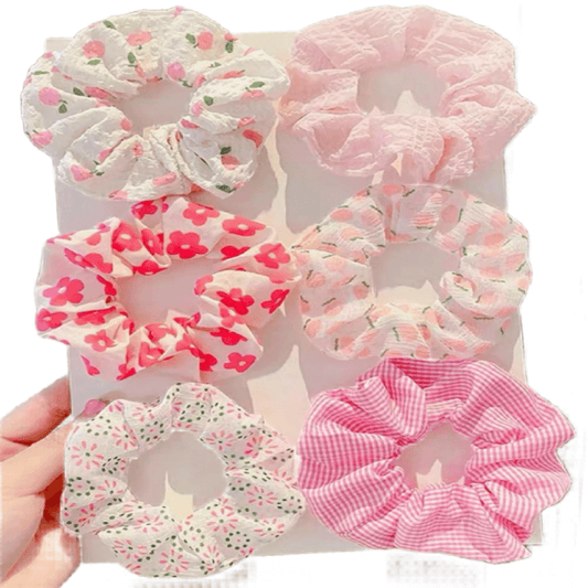 Set of pink and white scrunchies with floral patterns held by a hand.