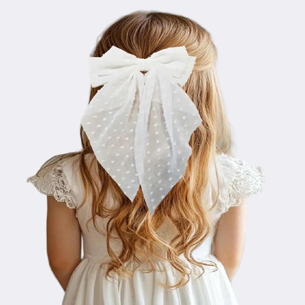 Person with long blonde hair wearing a large white polka dot bow in their hair, against a textured wall.