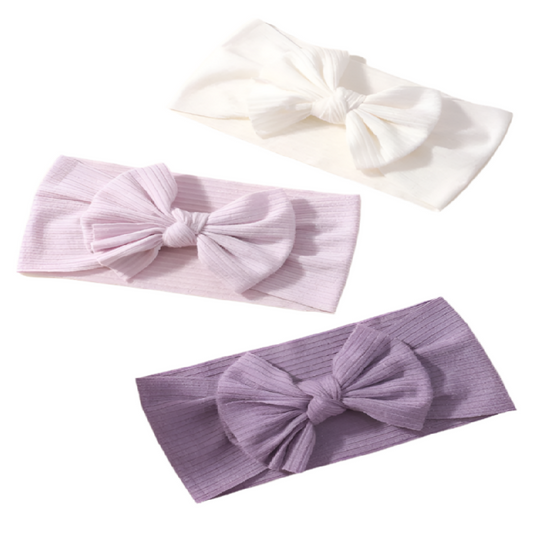 Three headbands with large bows in white, pink, and purple on a white background