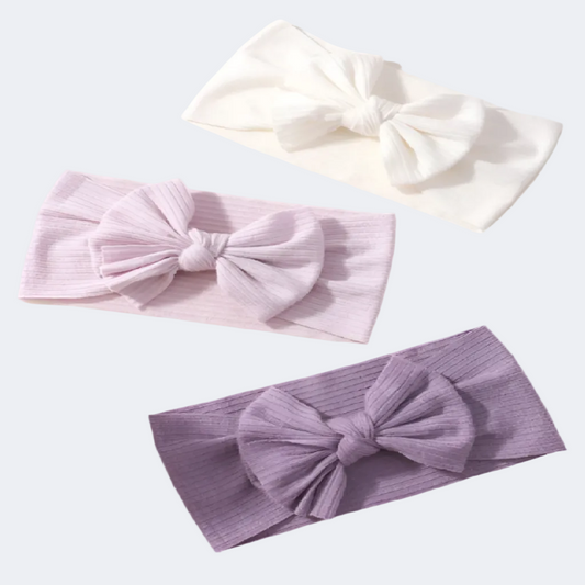 Three headbands with large bows in white, pink, and purple on a white background