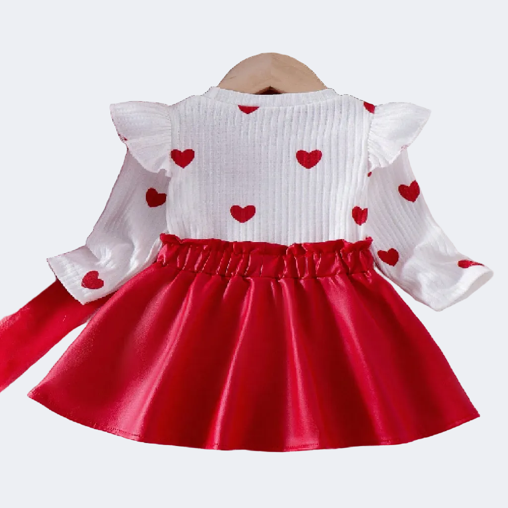 White top with red heart patterns and a red skirt on a textured surface with flowers and books.