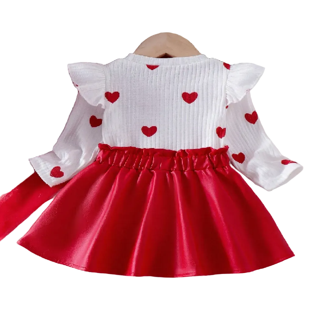 White top with red heart patterns and a red skirt on a textured surface with flowers and books.