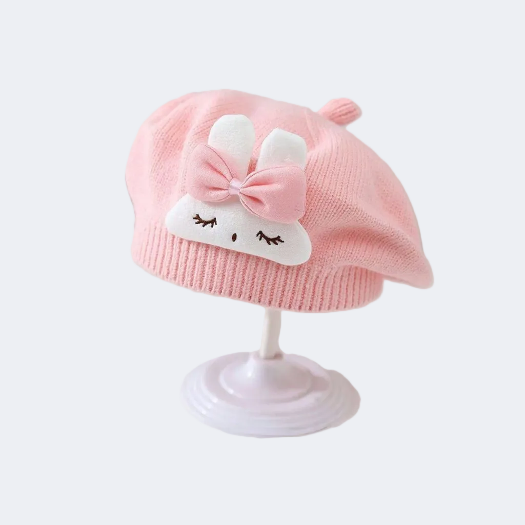 Pink baby hat with a bow and face design on a white background