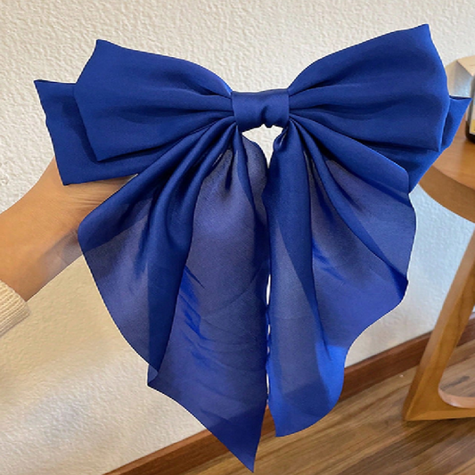 Large blue bow held by a hand against a neutral background
