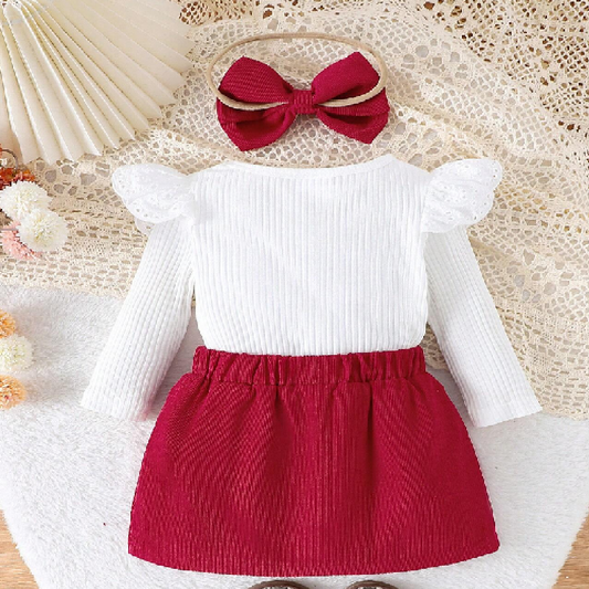 Children's outfit with white top and red skirt on a textured surface