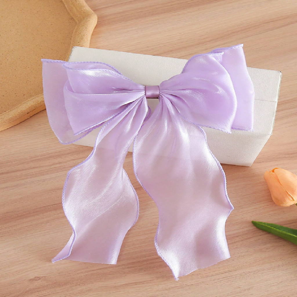 Large purple bow on a wooden surface with a white box and orange flower in the background