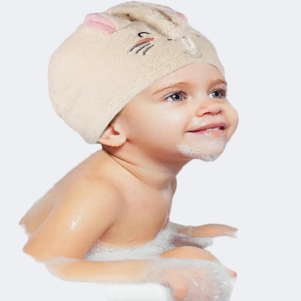 Child in a bathtub wearing a beige towel cap with cartoon face, smiling.