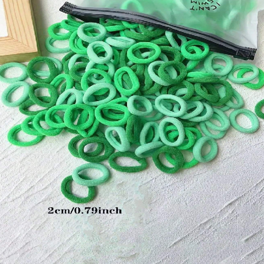 Green hair ties scattered on a textured surface with a clear plastic bag in the background.
