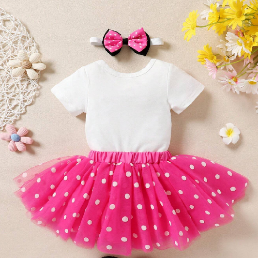 White top with pink polka dot skirt and headband on a beige background with flowers.