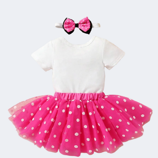 White top with pink polka dot skirt and headband on a beige background with flowers.