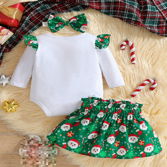 Christmas-themed baby outfit with white top, green skirt, and bow headbands on a wooden surface.