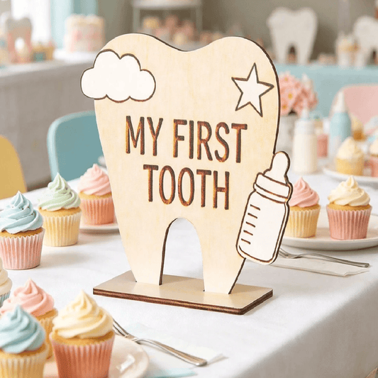 Wooden plaque with 'My First Tooth' text on a table with cupcakes