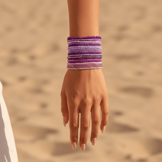 Hand wearing a purple bracelet against a sandy background