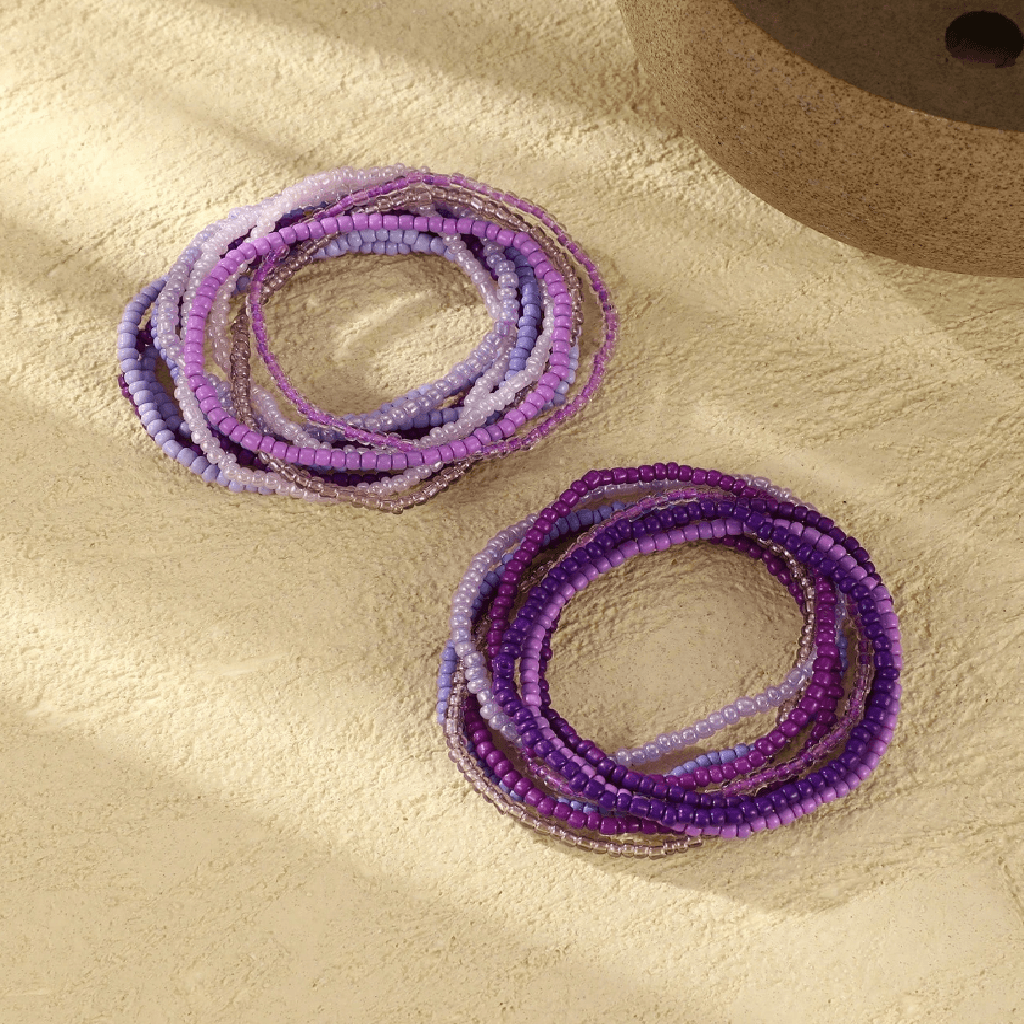 Set of purple beaded bracelets on a textured beige surface