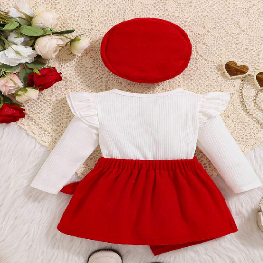 Children's outfit with white top and red skirt on a textured surface with flowers and heart-shaped objects.