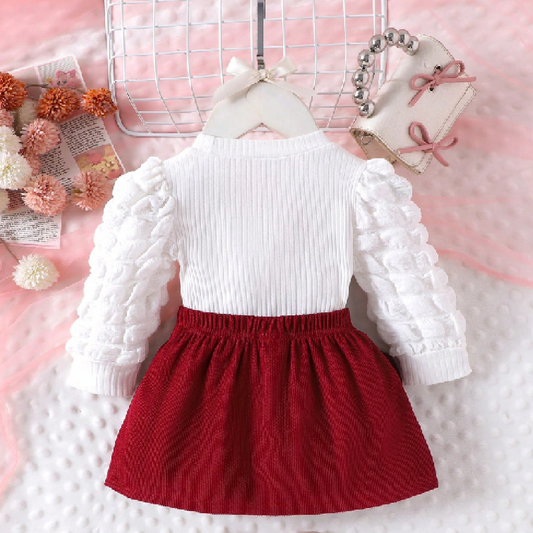 White long-sleeve top with ruffled details and a red skirt on a pink background