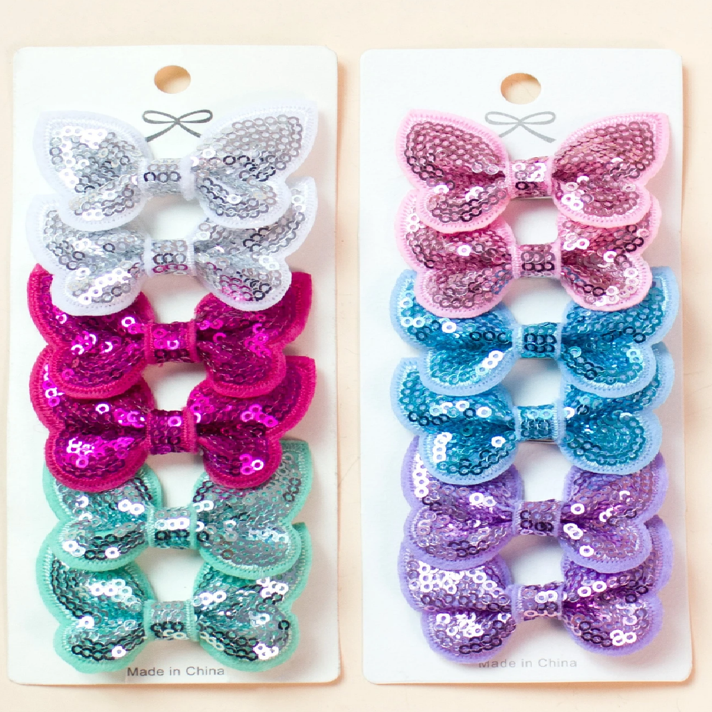 Two packages of sequin hair bows on a beige background