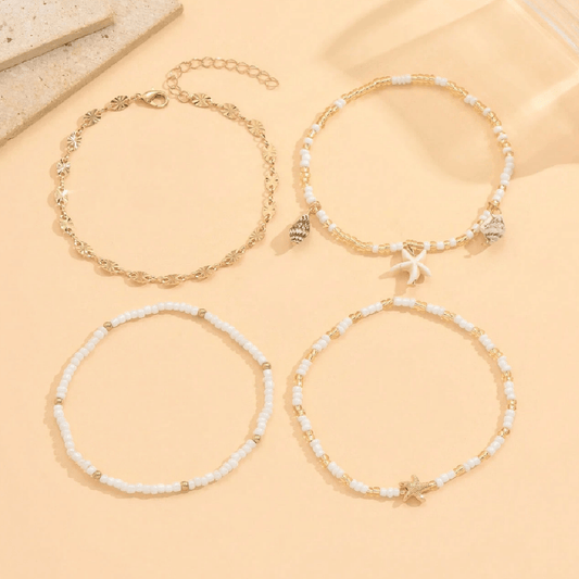 Set of four gold and white beaded bracelets on a beige surface