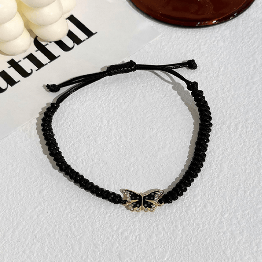 Black beaded bracelet with a butterfly charm on a light gray surface.