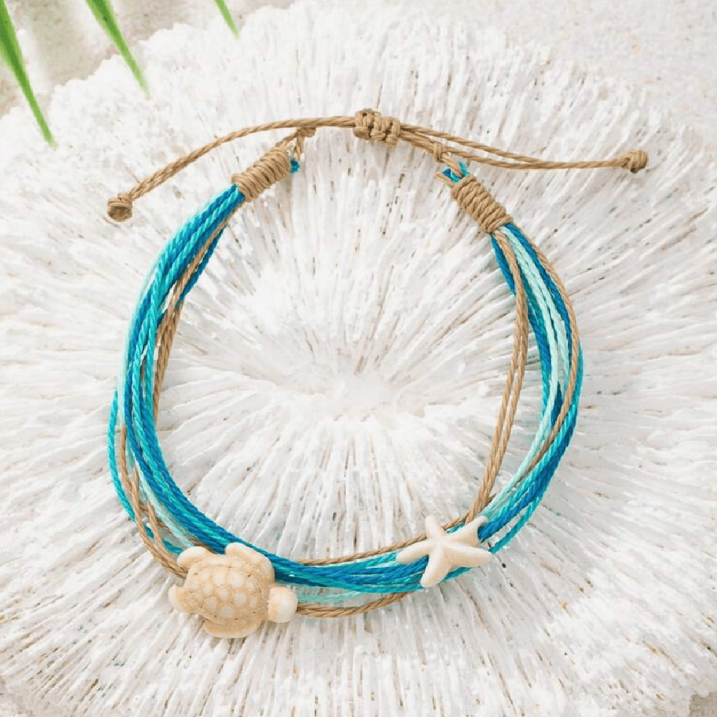 Multistrand bracelet with shell and starfish charms on a textured white surface