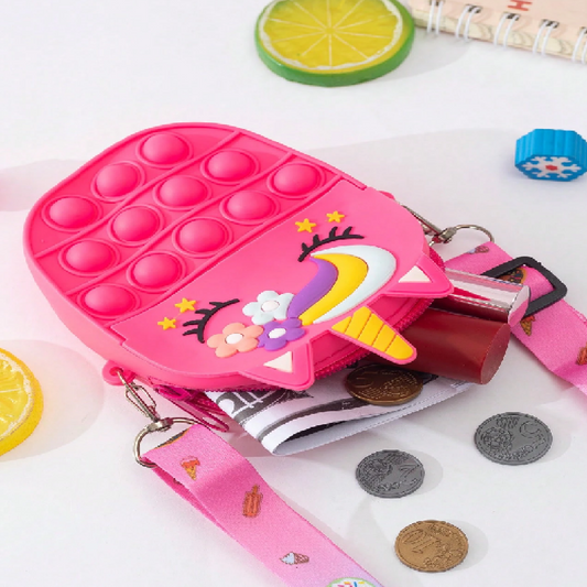 Pink unicorn-shaped pop-it fidget toy with coins and a magazine on a white surface.