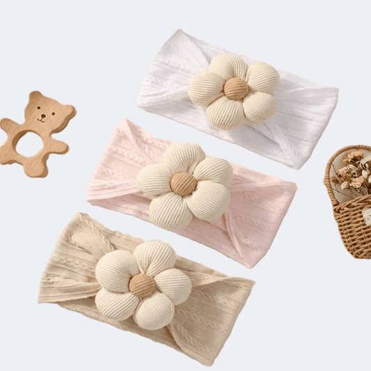 Three floral headbands in beige, pink, and white on a light background with a wooden bear toy and basket.