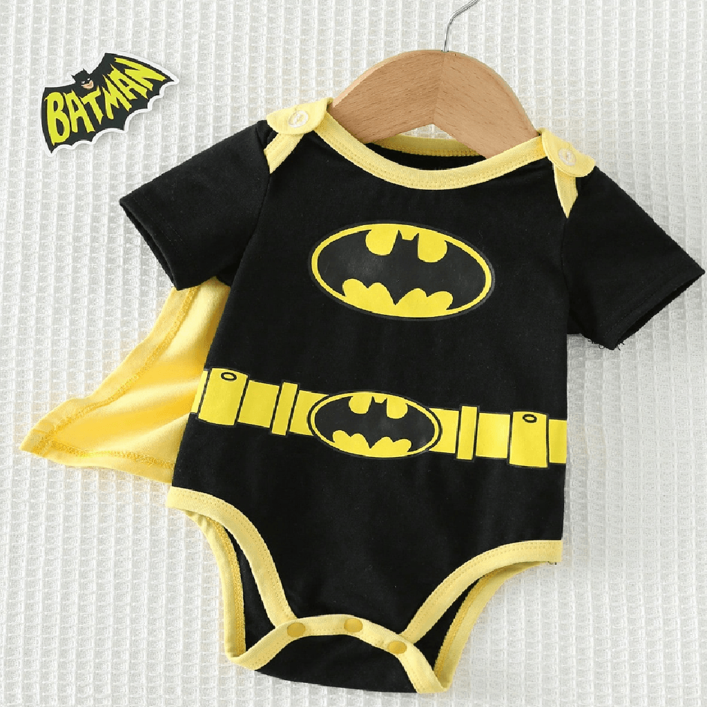 A baby short-sleeve bodysuit in black with yellow trim and Batman logo graphics, displayed on a wooden hanger with a yellow cape behind it. A Batman logo patch is shown in the top left corner.