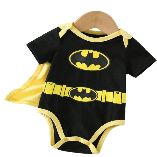 A baby short-sleeve bodysuit in black with yellow trim and Batman logo graphics, displayed on a wooden hanger with a yellow cape behind it. A Batman logo patch is shown in the top left corner.