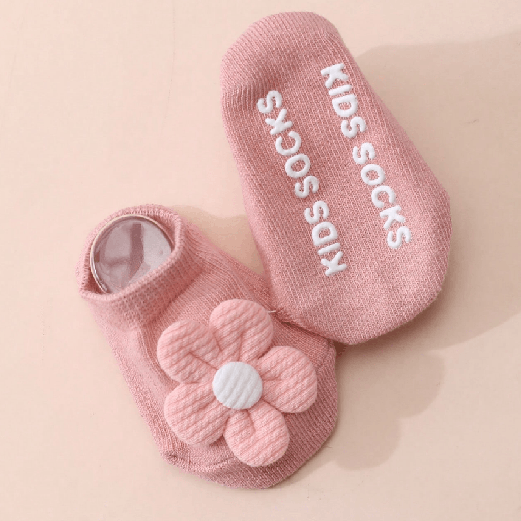 A pair of pink knit baby socks on a light beige background. One sock features a 3D pink flower applique with a white center, and the other sock has 'KIDS SOCKS' printed in white text.