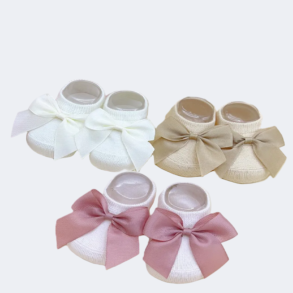 Set of baby shoes with bows in white, beige, and pink on a floral background.