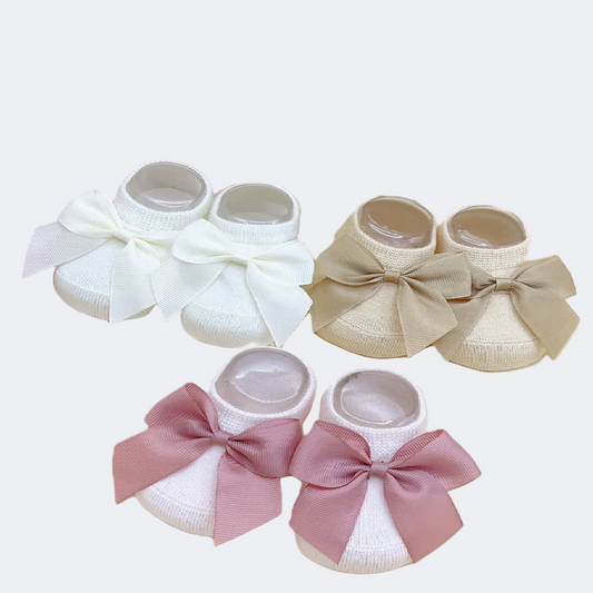 Set of baby shoes with bows in white, beige, and pink on a floral background.