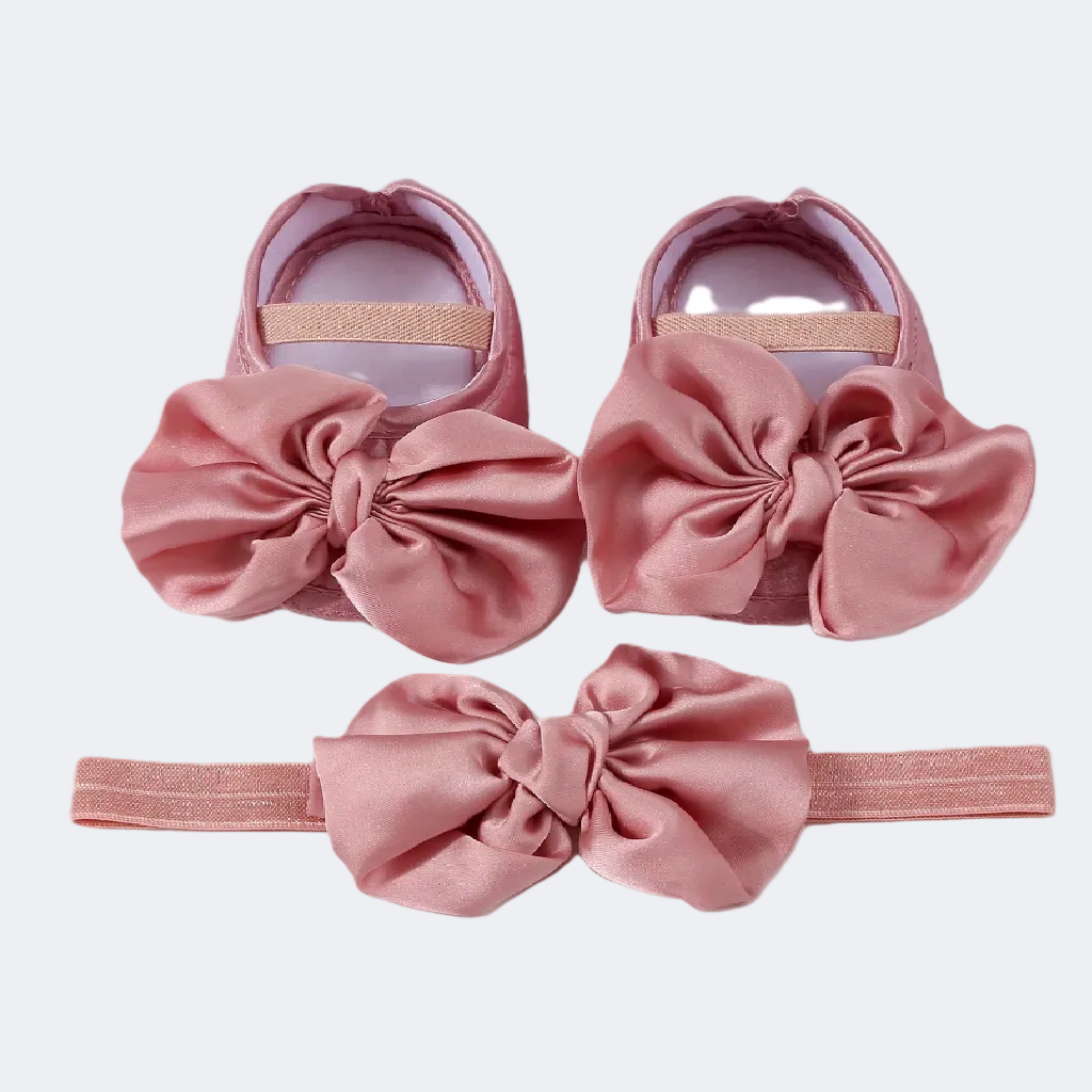 Set of pink baby shoes and headband with large bows on a white background