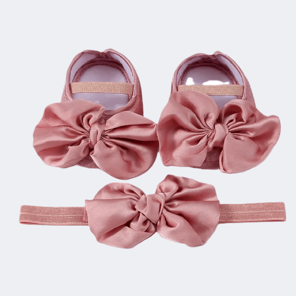 Pink baby shoes and headband set on a light purple background