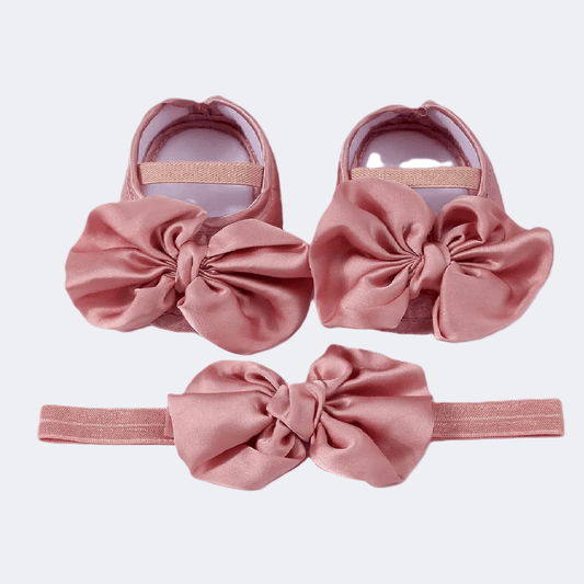 Pink baby shoes and headband set on a light purple background