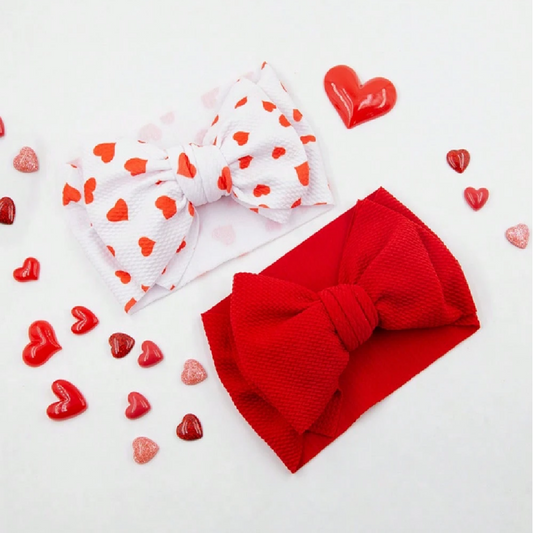 Two headbands, one red with a bow and one white with red heart patterns