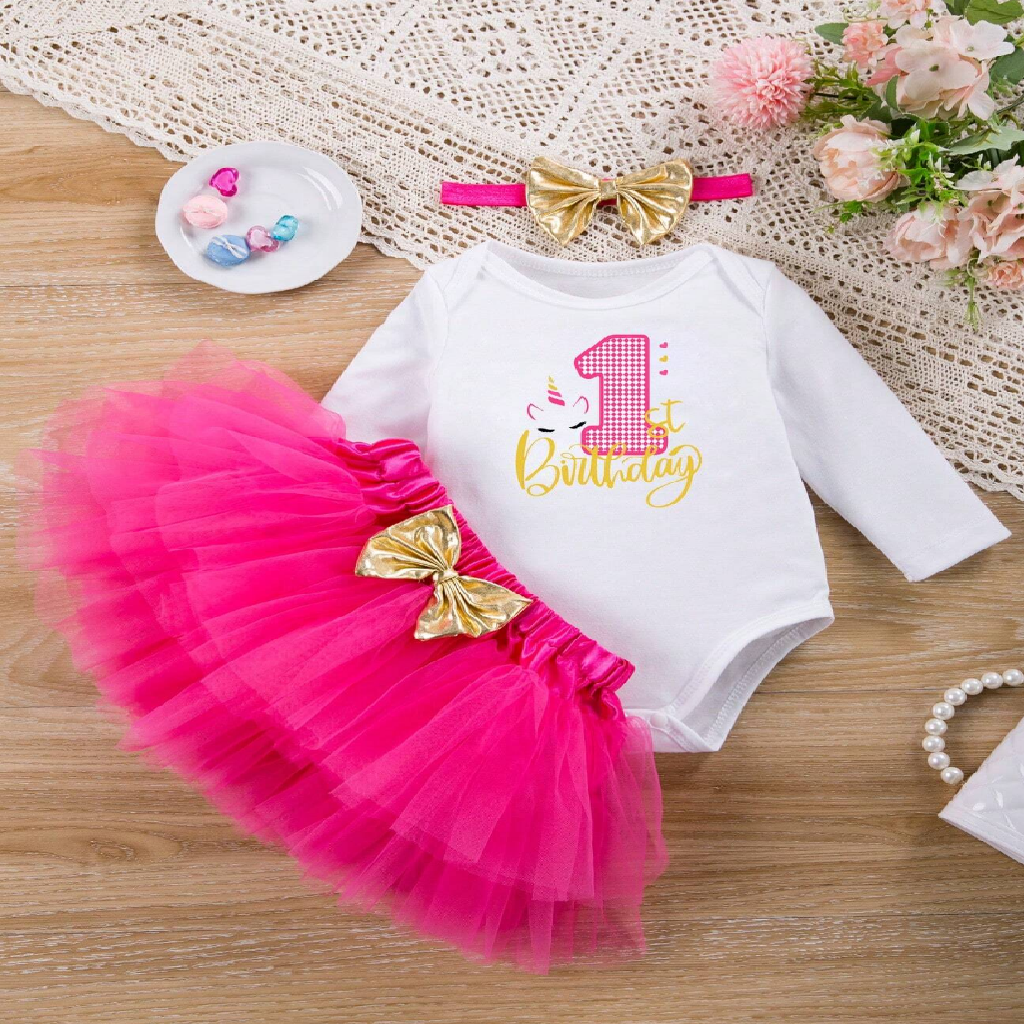 Baby outfit with pink tutu, white long-sleeve shirt, and gold bow on a wooden surface.