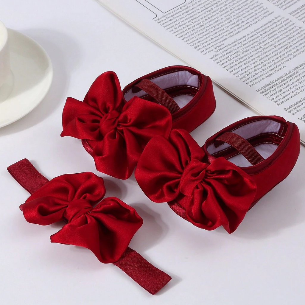 Red baby shoes with large bows on a white surface