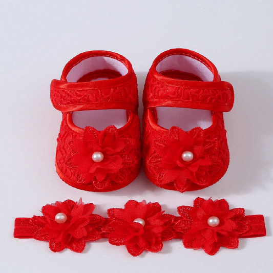 Red baby shoes with floral designs and pearl embellishments on a white background