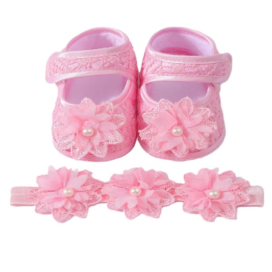 Pink baby shoes with floral designs and a matching headband on a white background