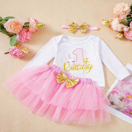Baby outfit with pink tutu, white long-sleeve top with gold text, and matching headband on a beige background with flowers.