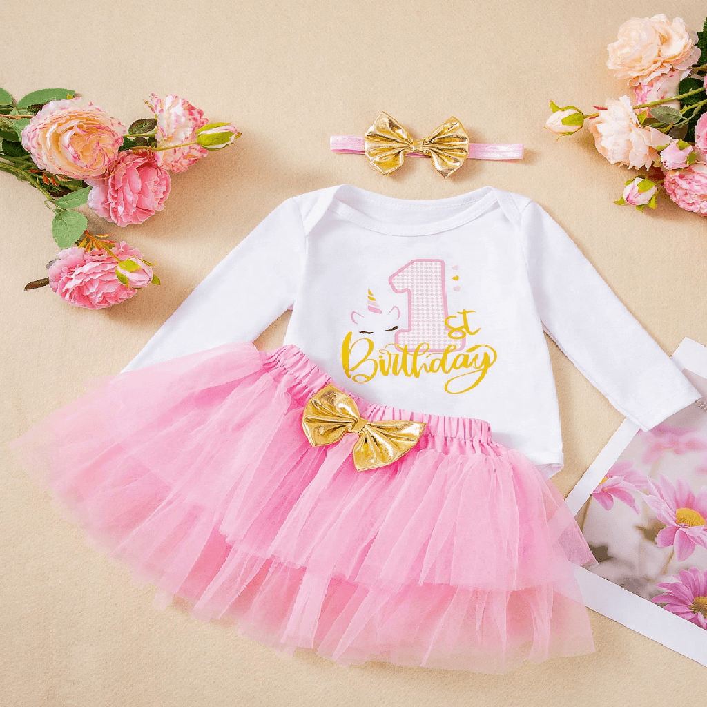 Baby outfit with pink tutu, white long-sleeve top, and gold accents on a beige background with flowers.